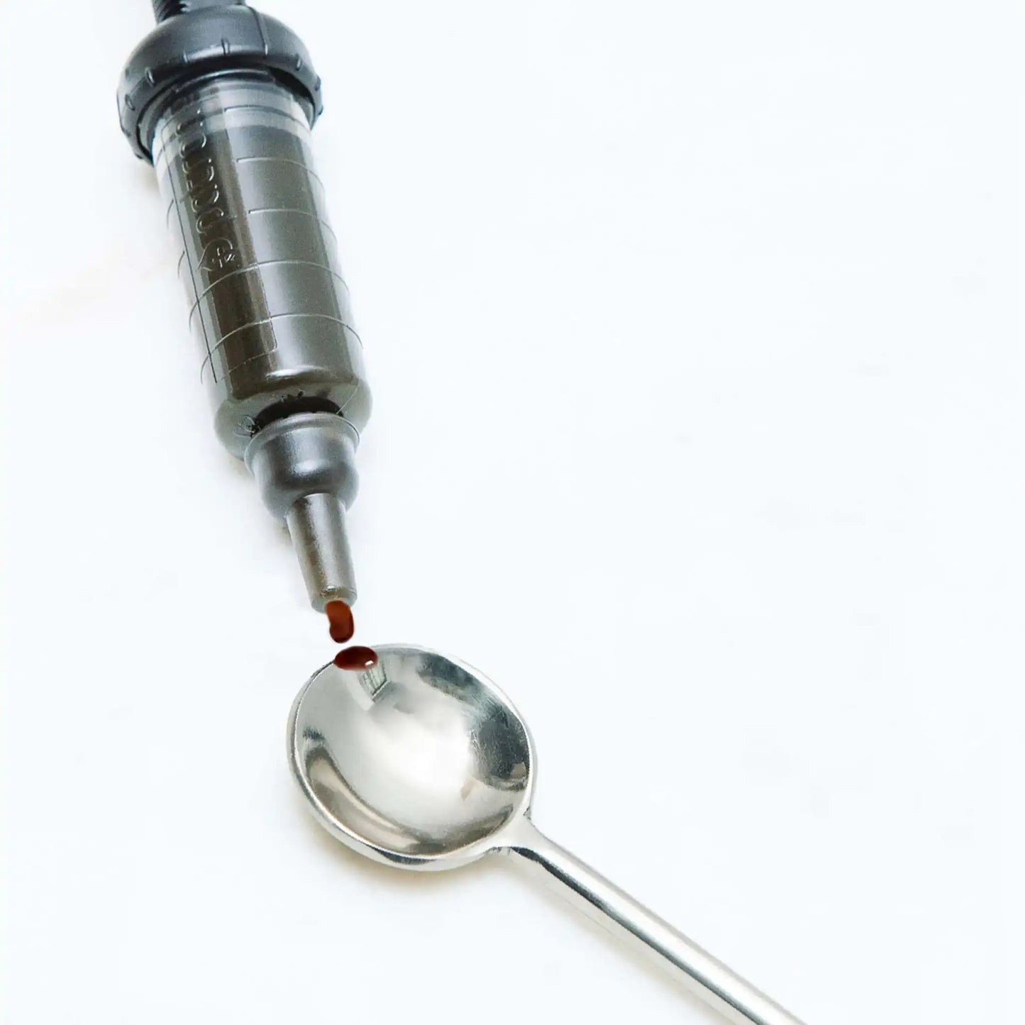 Ruiskumainen annostelulaite tiputtaa punaisen nesteen lusikkaan.