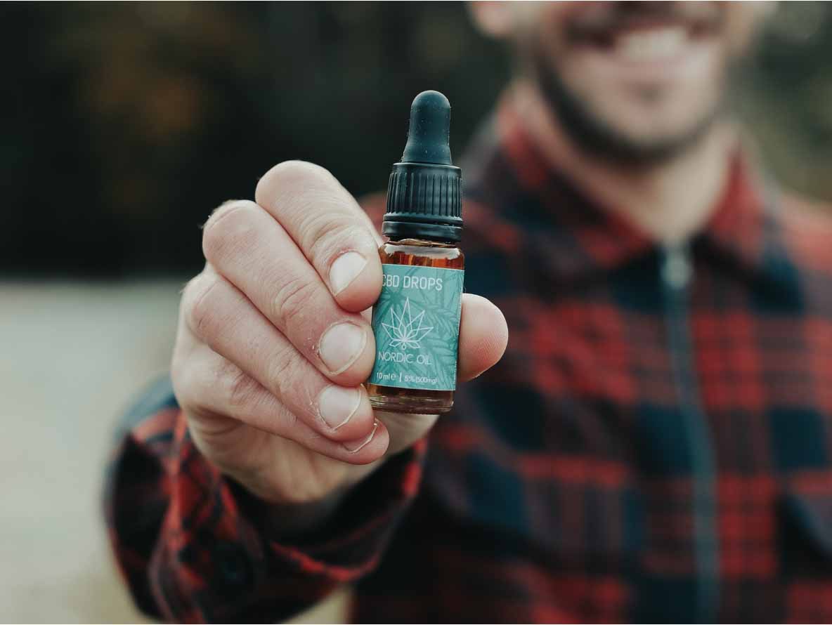 Henkilö pitää kädessään CBD-tippoja sisältävän pullon, jossa on turkoosi etiketti.
