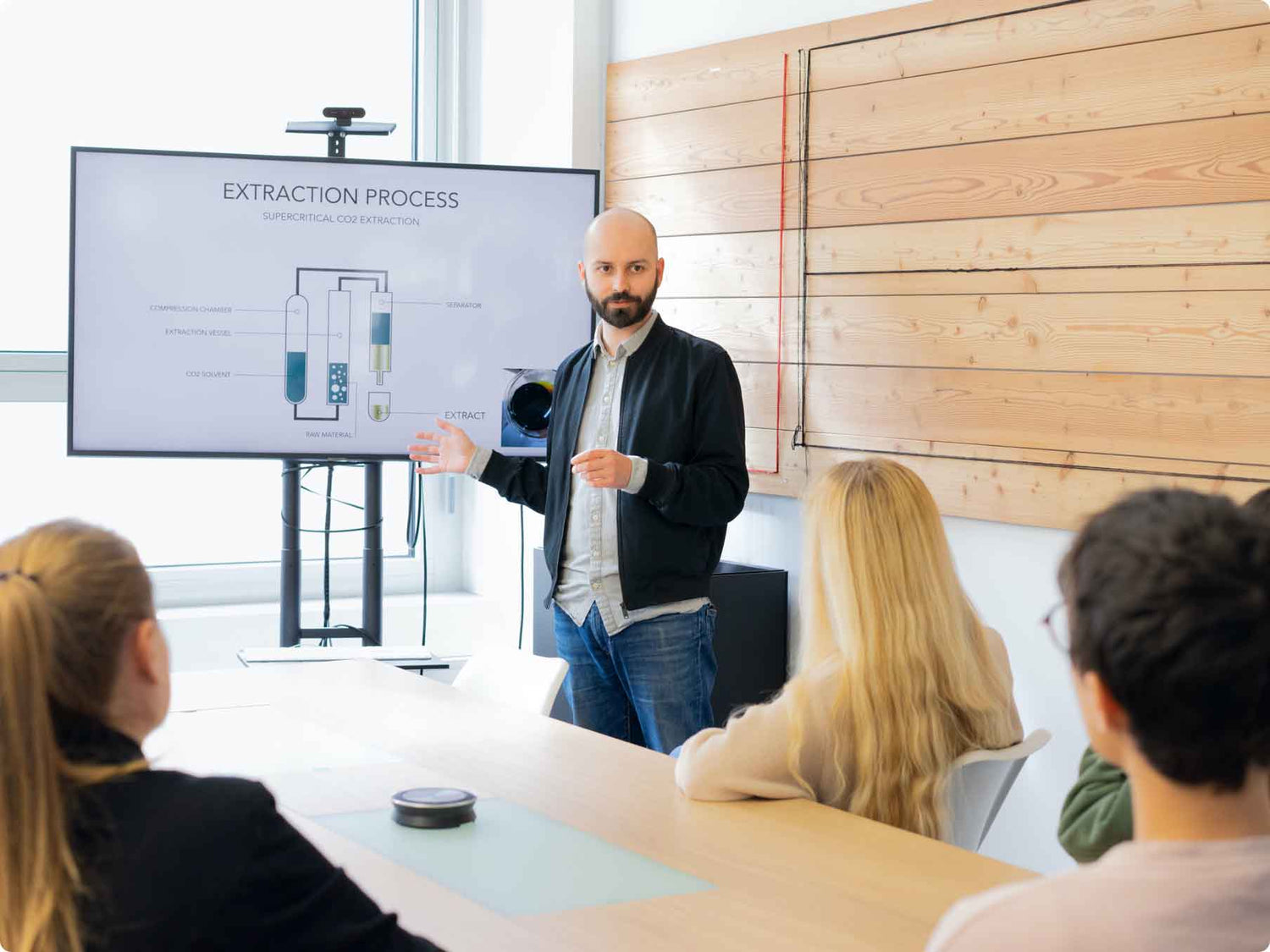 Mies esittelee CO2-uuttamisen prosessin kaavioita suurella näytöllä luokkahuoneessa, yleisö seuraa.
