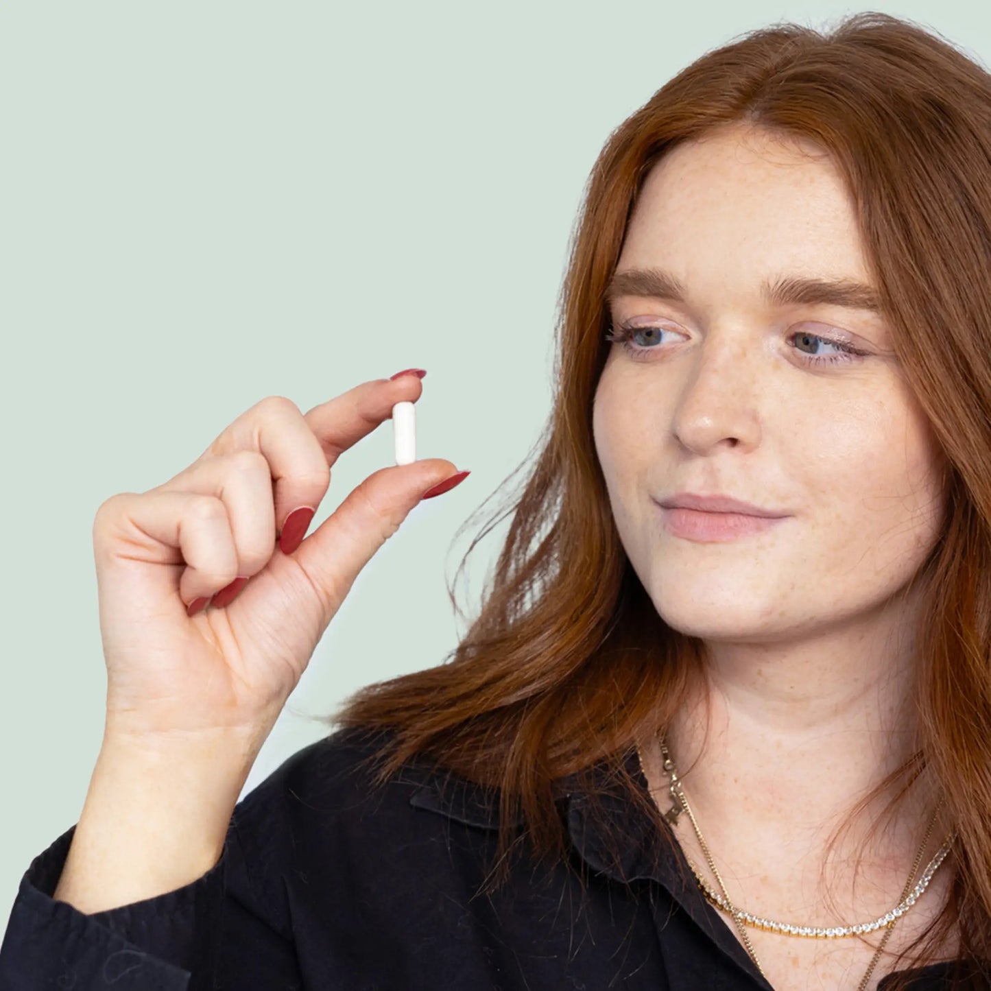 Nainen pitää kädessään pientä valkoista kapselia.