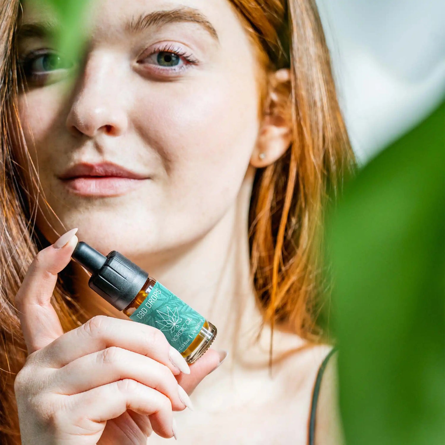 Nuori nainen, jolla on kädessään 10ml laajakirjoista CBD-öljyä