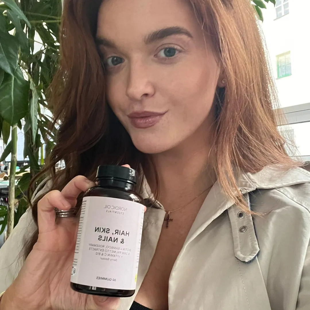 Nainen hymyilee ja pitää kädessään pullon Hair, Skin & Nails -lisäravinnetta.